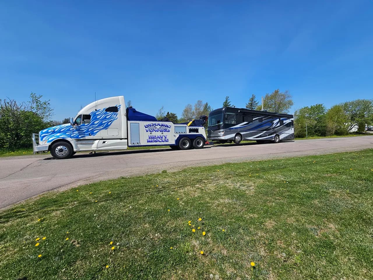 Dynamic Towing heavy-duty wrecker towing a large motorhome on a sunny New Brunswick lot