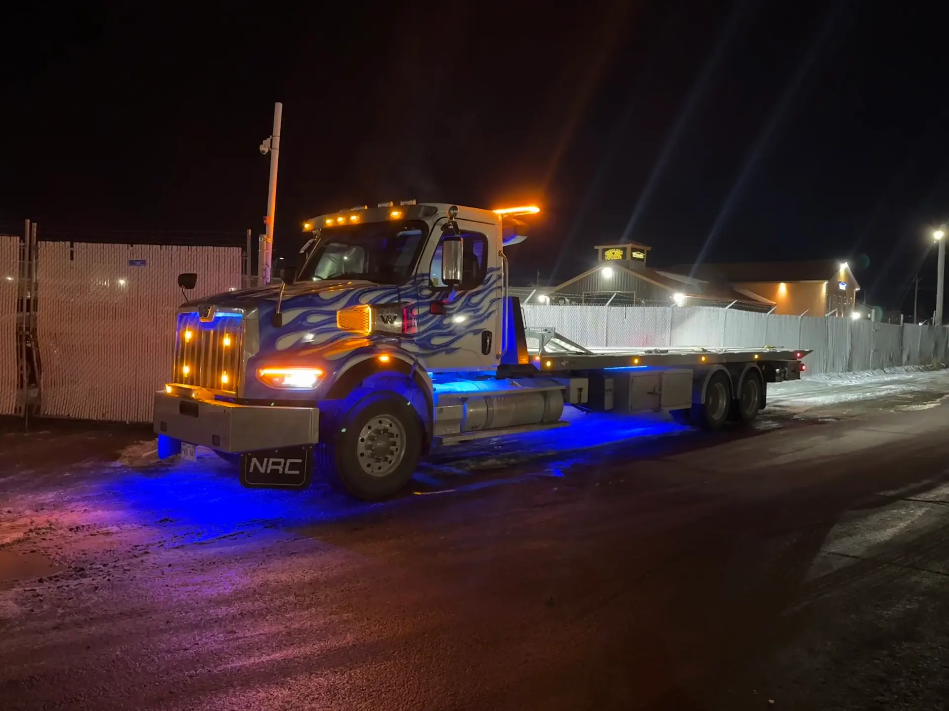 Dynamic Towing flat-deck tow truck at night with blue underglow lighting